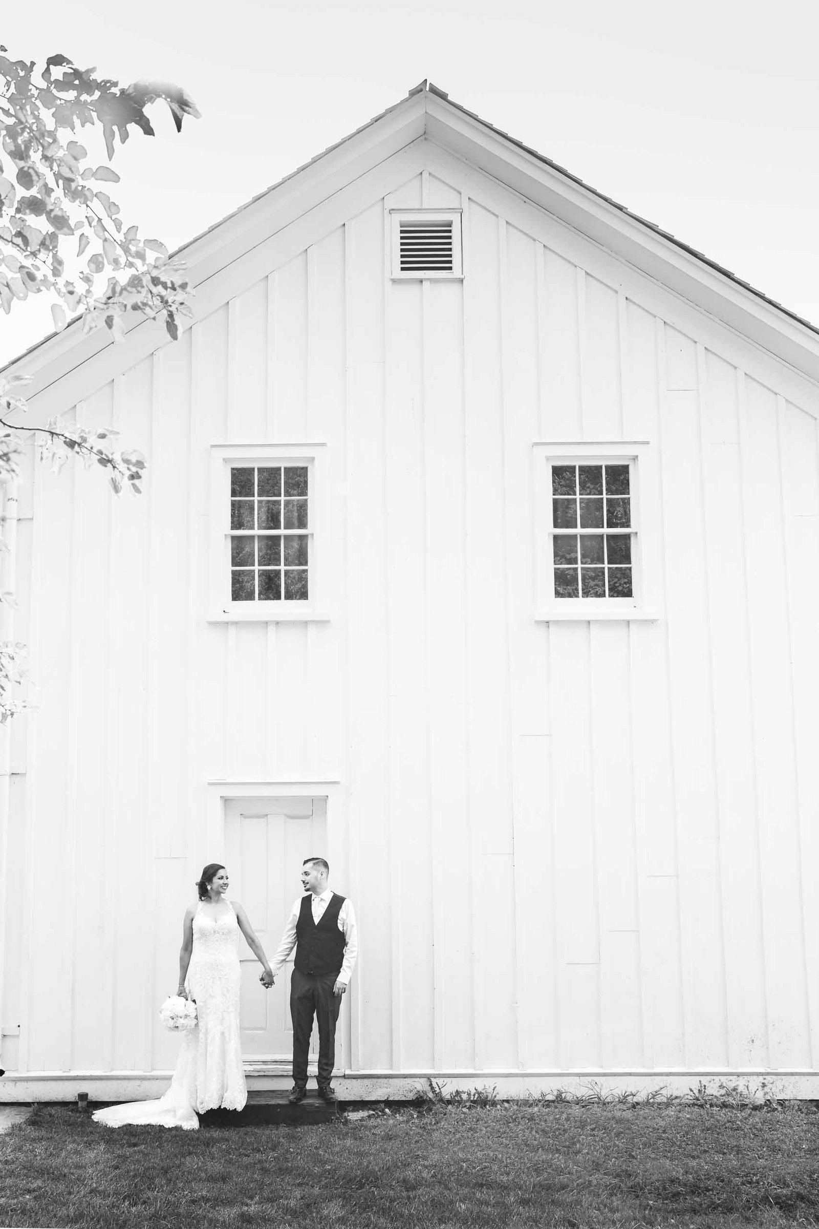bride and groom standing against an old white house